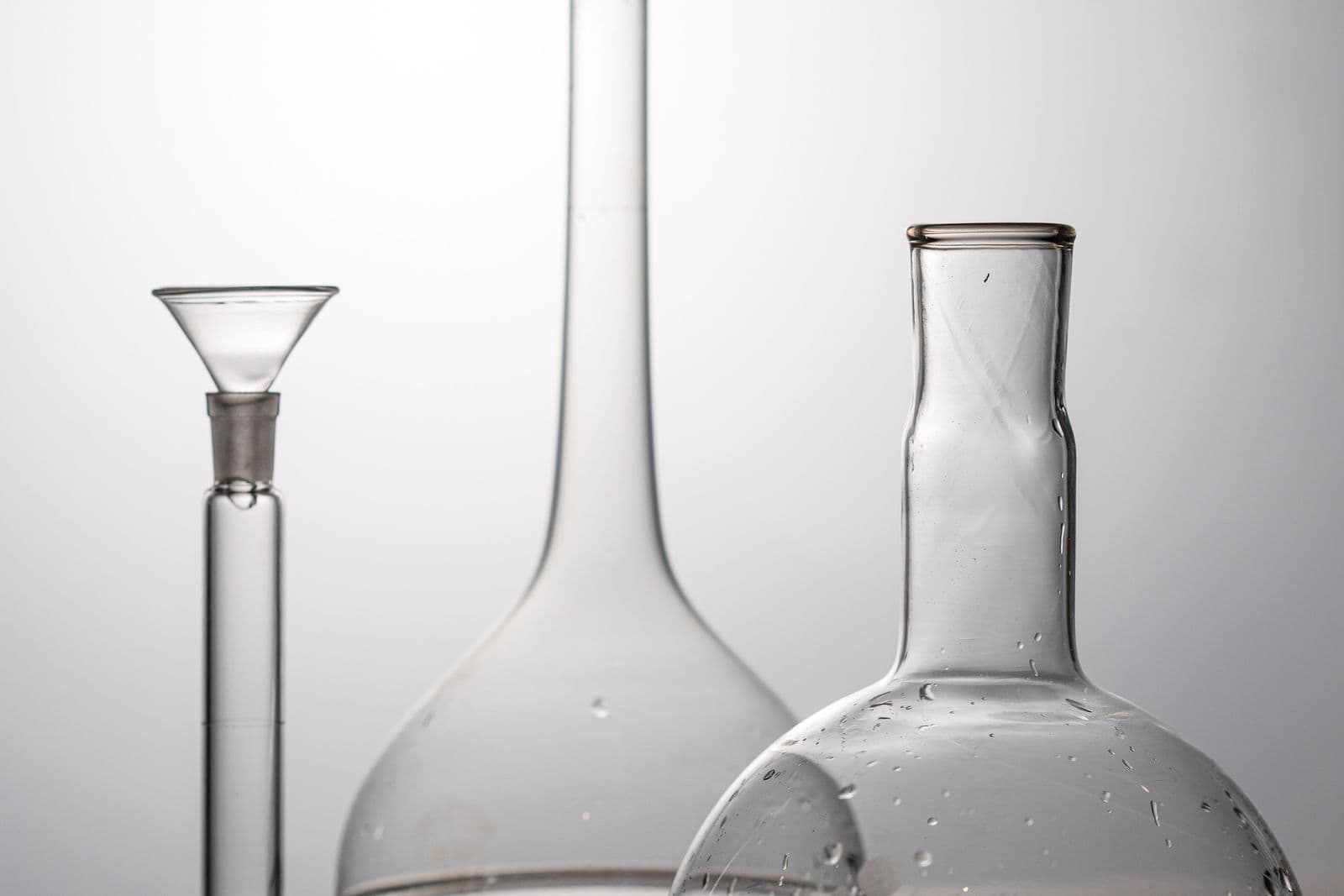 Three clean laboratory flasks with clear liquid on a wooden surface in soft studio light.